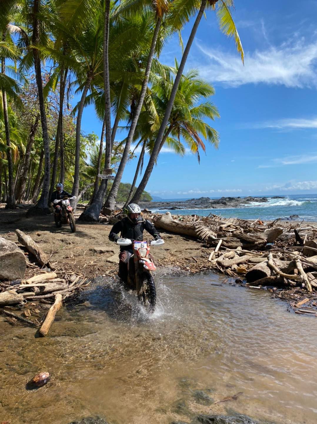 Two Dirtbike Tours Costa Rica riders crossing water beside the Pacific coast