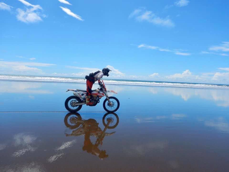 A dirtbike rider travelling across a reflective Pacific beach in Costa Rica